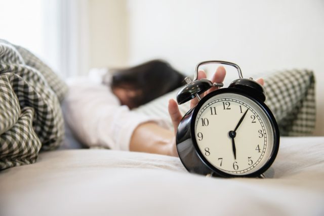 sleepy woman reaching holding alarm clock
