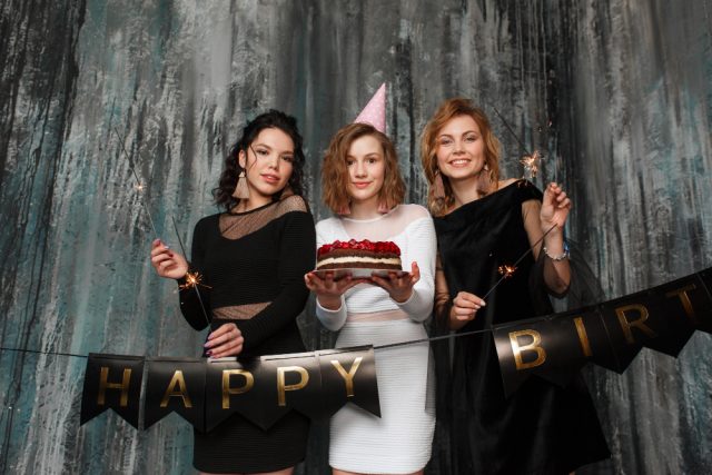 three young beautiful girls celebrate birthday holding cake sparklers